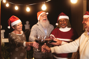 Happy senior friends celebrating Christmas holidays while toasting with red wine glasses on house patio party