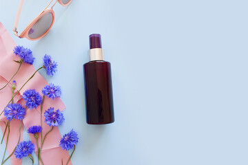 Mockup of brown spray bottle, blue wild flowers, pink sunglasses and pink silk ribbon on pastel blue background. Bottle for branding and label. Natural organic cosmetics