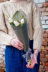 Bouquet of flowers in striped black and pistachio-colored package in hands.