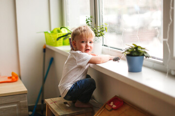 A lonely sad toddler toddler looks out the window with tears, a child in kindergarten without a...
