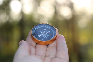 Old classic navigation compass in hand on natural background with bokeh as symbol of tourism with...