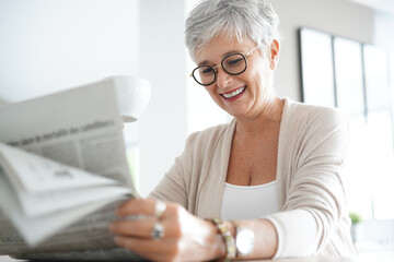 Portrait of smiling mature woman at home reading newspaper