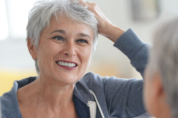 Senior woman with short grey hair putting make-up on