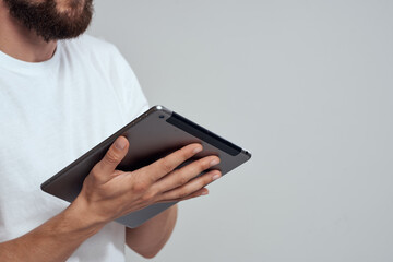 Tablet with a touch screen on a light background male hands white t-shirt cropped view