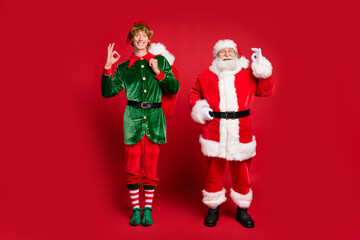 Full length photo of two character santa elf hold sack show okey wear x-mas costume cap glasses...