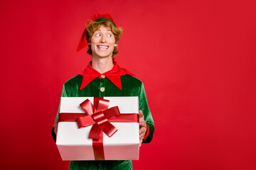 Photo of elf helper hold present look side empty space wear green x-mas costume cap isolated red color background