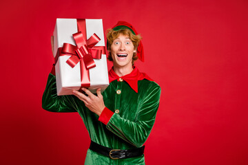 Photo of amazed ginger elf hold gift open mouth amazed wear green x-mas costume headwear isolated...