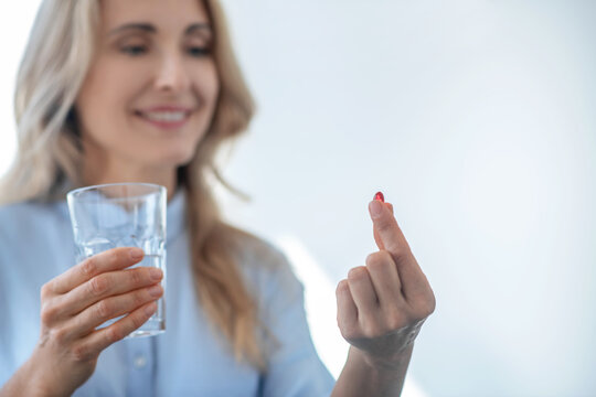 Blonde Female Holding Glass Of Water, Taking Red Pill