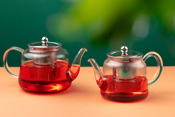 Glass teapot with black tea on background of blurred foliage