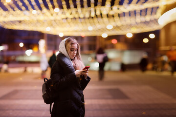 Caucasian young girl woman in winter coat with phone on the street, communication holidays, safety