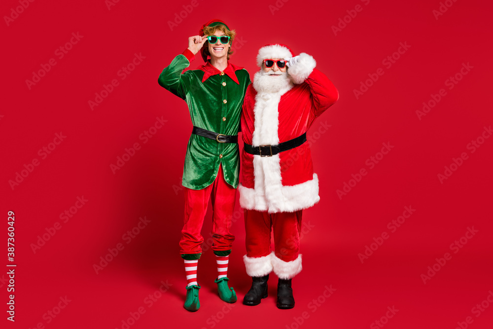 Wall mural Full length photo of two people elf santa claus hug wear x-mas costume sunglass coat cap boots isolated red color background