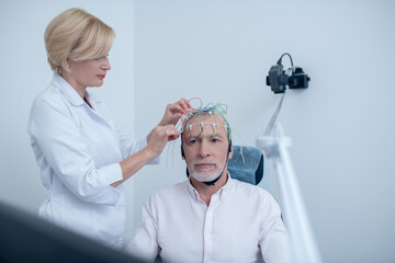 Female neurologist adjusting electrodes on gray-haired male patient head