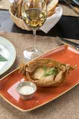 Baked trout in parchment stuffed with vegetables and glass of white wine on the table at restaurant