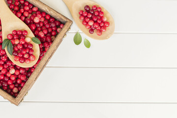 ripe cranberries in a wooden box and spoons on a white background view from above. background with cranberries on the table view above.
