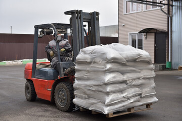 Forklift moves pallet with white bags outdoors