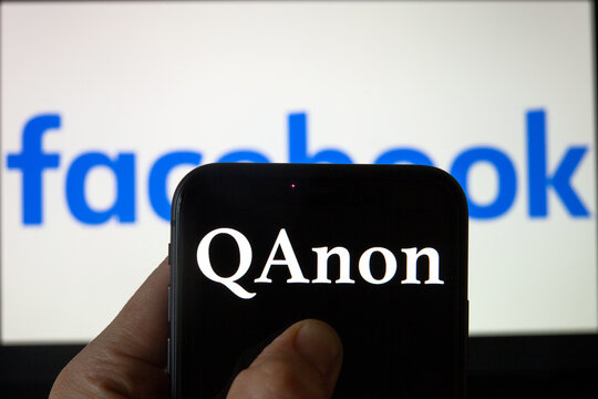 QAnon vs FACEBOOK. QAnon organization logo seen on the smartphone which is placed on Facebook logos. Concept for ban of QAnon on social media. 