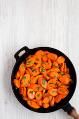 Homemade Sauteed Carrots in a cast iron pan on a white wooden background, overhead view. Flat lay, top view, from above. Copy space.