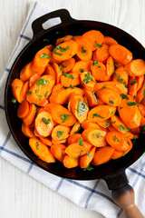 Homemade Sauteed Carrots in a cast iron pan on a white wooden surface, top view. Flat lay, overhead, from above. Close-up.