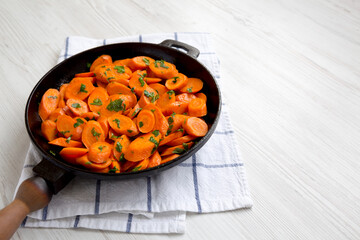 Homemade Sauteed Carrots in a cast iron pan on a white wooden surface, side view. Copy space.