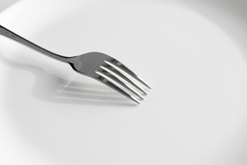 Metal fork lying on a white plate, close-up. Concept: nothing more, hunger.