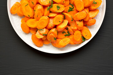 Homemade Sauteed Carrots on a plate on a black surface, top view. Flat lay, overhead, from above. Space for text.
