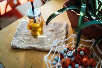 Vaso calavera con liquido naranja junto a dulces de halloween y plantas verdes