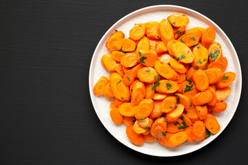 Homemade Sauteed Carrots on a plate on a black surface, top view. Flat lay, overhead, from above. Space for text.