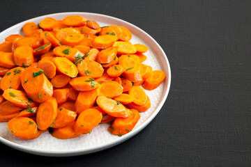 Homemade Sauteed Carrots on a plate on a black background, side view. Copy space.