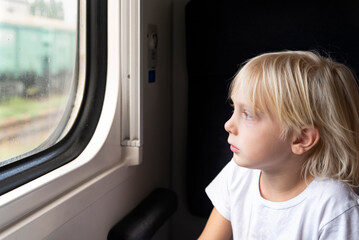 Fototapeta na wymiar Blond boy looks thoughtfully out the train window. Rail travel