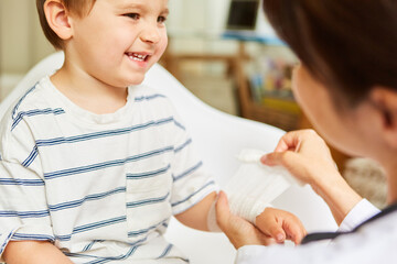 Kinderarzt bindet Mullbinde um Handgelenk von Kind