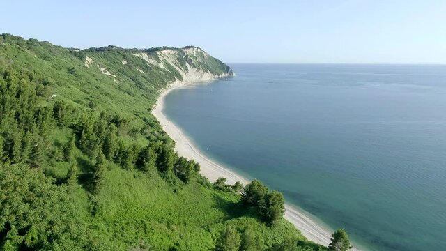 Aerial bird's eye view taken by drone of Mezzavalle beach near Portonovo. The wild beach under a steep cliff with green vegetation reflected in the water is a very famous tourist destination in Marche