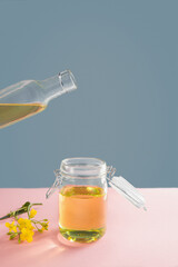 Vegetable oil from rape in a glass jar and a bottle on a pink-gray background