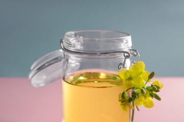 Vegetable oil from rape in a glass jar on a pink-gray background, a close up
