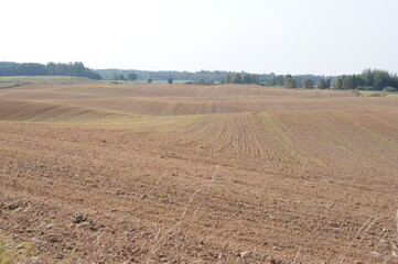A farmable hilly farm landscape with field after harvest in autumn with brown soil