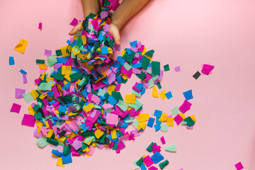 Children's hands scatter colorful confetti. Top view, horizontally on a pink background, with space