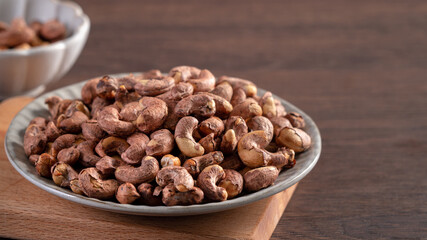 Cashew nuts with peel in a plate on wooden tray.