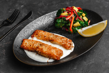 Pan-fried barramundi or pangasius. Breaded fish steak with sesame seeds and lemon sour cream. With avocado salad and Kale leaves. healthy eating style