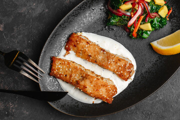 Pan-fried barramundi or pangasius. Breaded fish steak with sesame seeds and lemon sour cream. With avocado salad and Kale leaves. healthy eating style