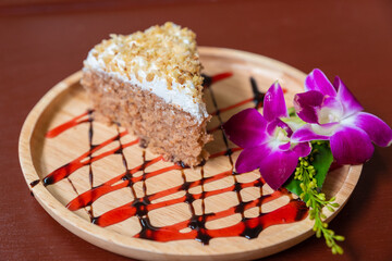 vegan and vegetarian sponge cake with nuts and maple chocolate syrup decorated with orchid flowers, handmade cake on a wooden plate in a restaurant,  white cream