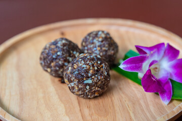handmade vegan and vegetarian sweets, Asian traditional cuisine, three delicious dried fruit balls wrapped in nuts and decorated with an orchid flower on a wooden plate in a restaurant