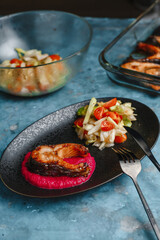 Trout. Baked salmon steaks on a beetroot pillow with vegetable salad, cucumber, tomato, onion, lettuce. Side view, top view.