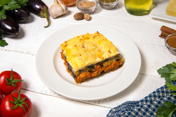 Greek Moussaka close up in dish with the ingredients on the white rustic table.