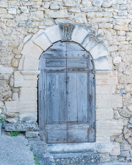 Fototapeta na wymiar Porte traditionnelle en bois avec des pierres taillée encadrée par un mur en pierres apparentes dans un village du Lubéron en France un jour ensoleillé