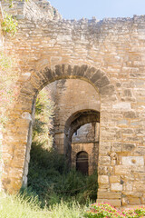 Fototapeta na wymiar Porte en pierre traditionnelle avec de longs murs et des bâtiments en pierres anciens en ruines dans le Lubéron un jour ensoleillé.