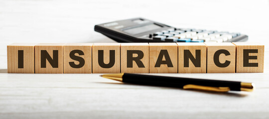 The word INSURANCE is written on wooden cubes between a calculator and a pen. Business concept.