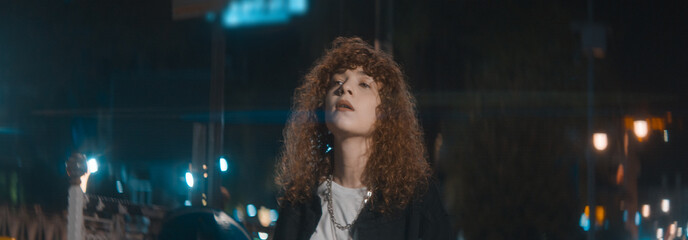 Unhappy attractive woman with curly hair in white t-shirt and black jacket is walking on the street...