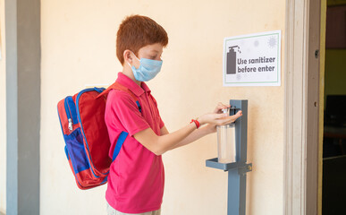 Fototapeta na wymiar Kid with medical mask using hand sanitizer before entering classroom - concept of back to school or school reopen and coronavirus or covid-19 safety measures.