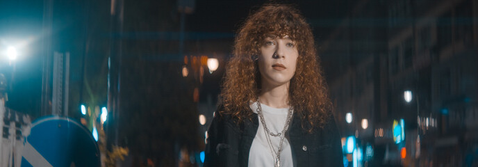 Unhappy attractive woman with curly hair in white t-shirt and black jacket is walking on the street...