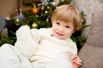 boy in white warm winter sweater with white Teddy bear in Christmas tree background. happy wide smile