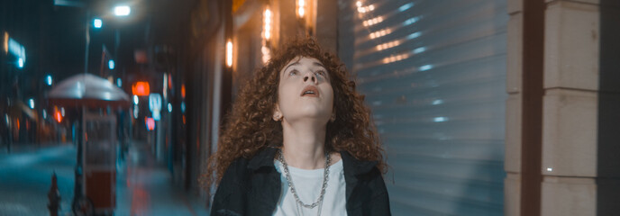 Stressful unhappy young attractive woman with curly hair in white t-shirt and black jacket is...